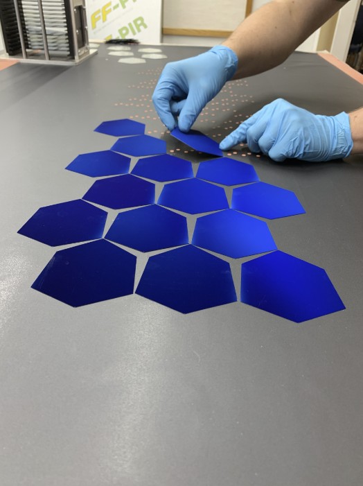 Gloved hands placing hexagonal blue solar cells on a work surface